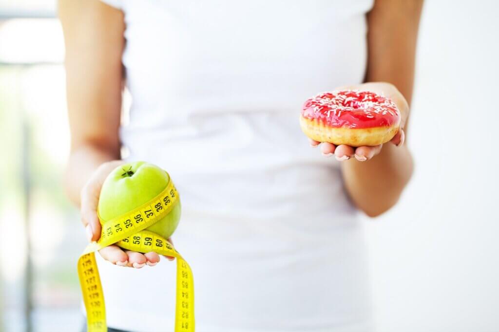 Diet concept, woman holding a choice of harmful donut and fresh apple.