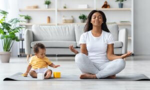 Mental Wellness Concept. Calm Happy Black Mother Meditating With Baby At Home